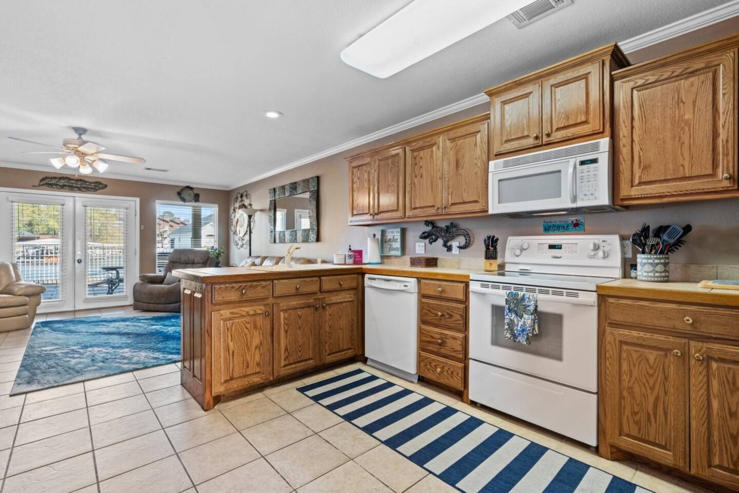 A kitchen with wooden cabinets , white appliances , and a blue and white striped rug.