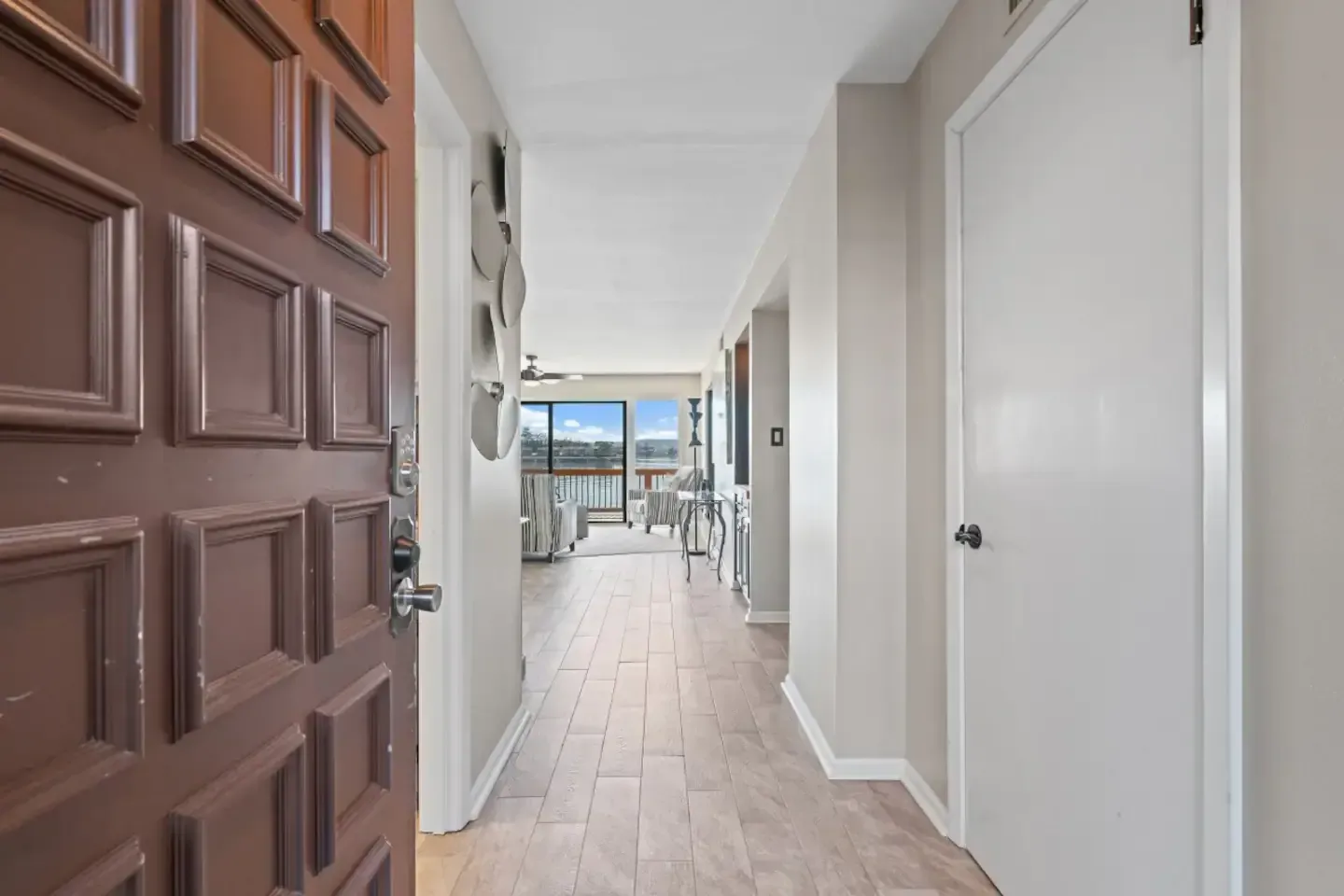 A hallway with a brown door and white doors leading to a living room.