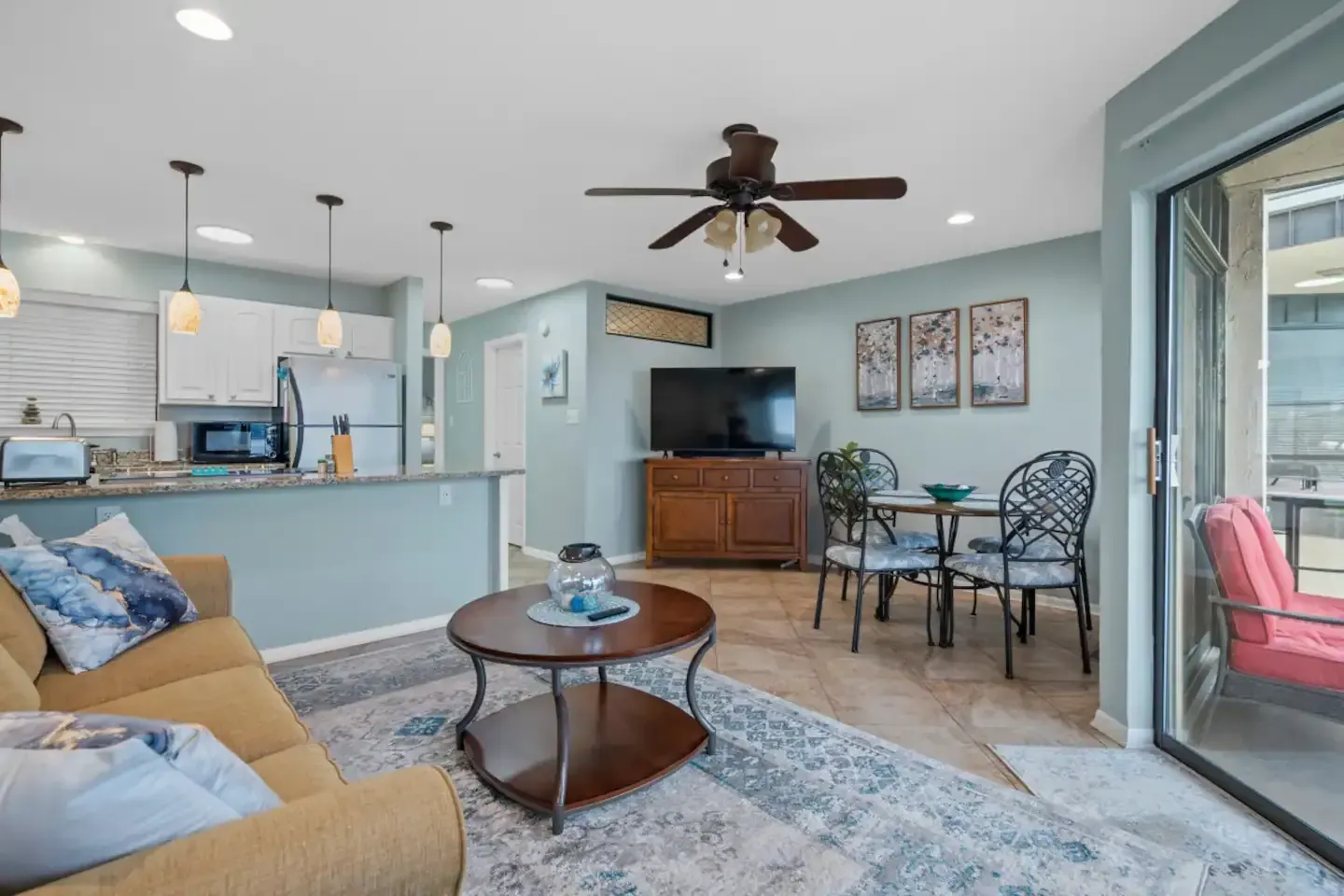 A living room with a couch , table , chairs , television and ceiling fan.