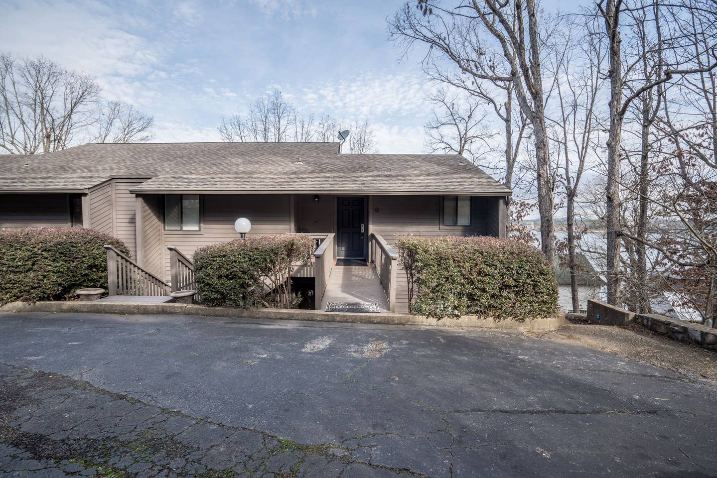 A large house with stairs leading up to it is surrounded by trees and bushes.