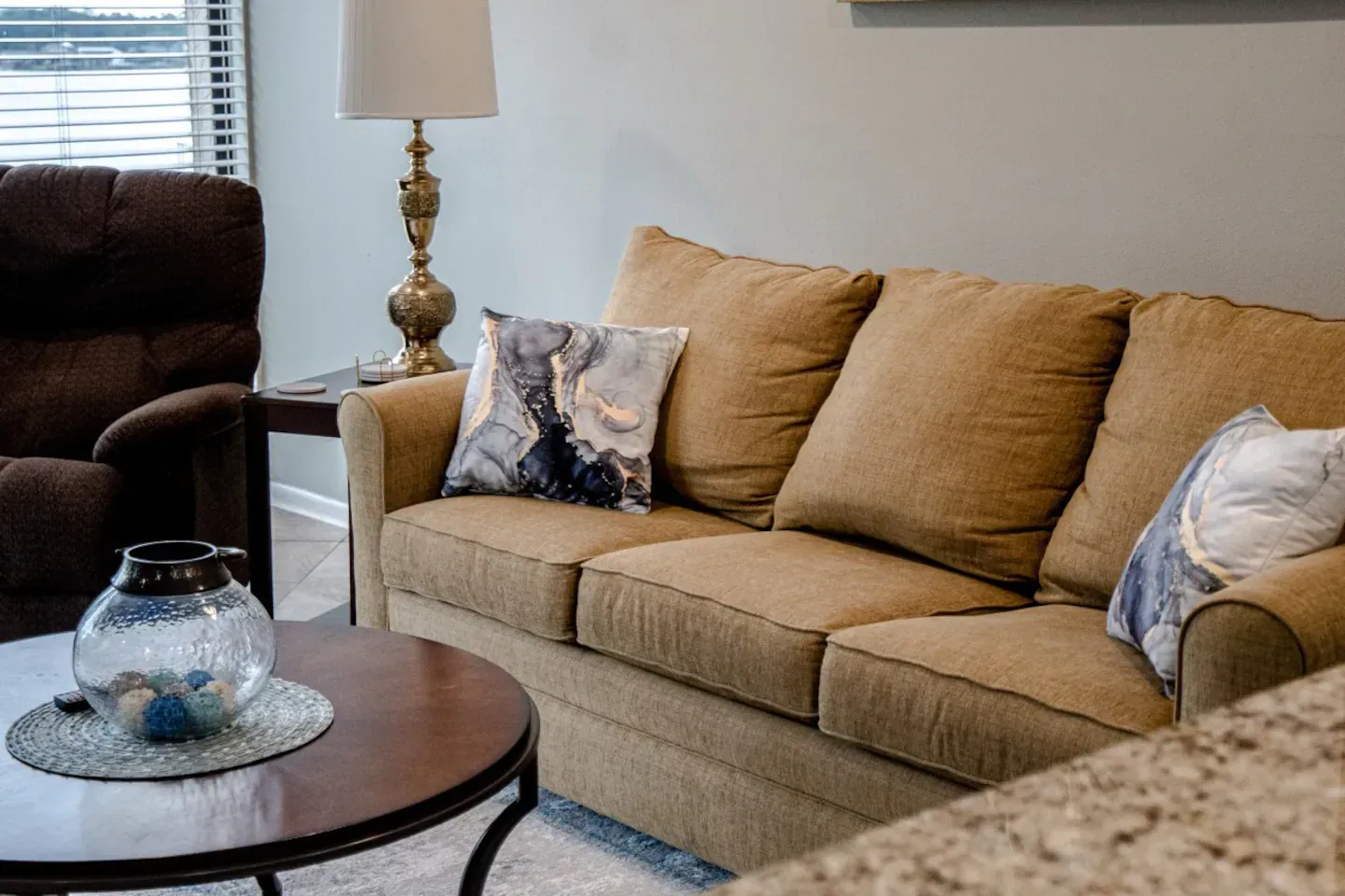A living room with a couch , chair , table and lamp.