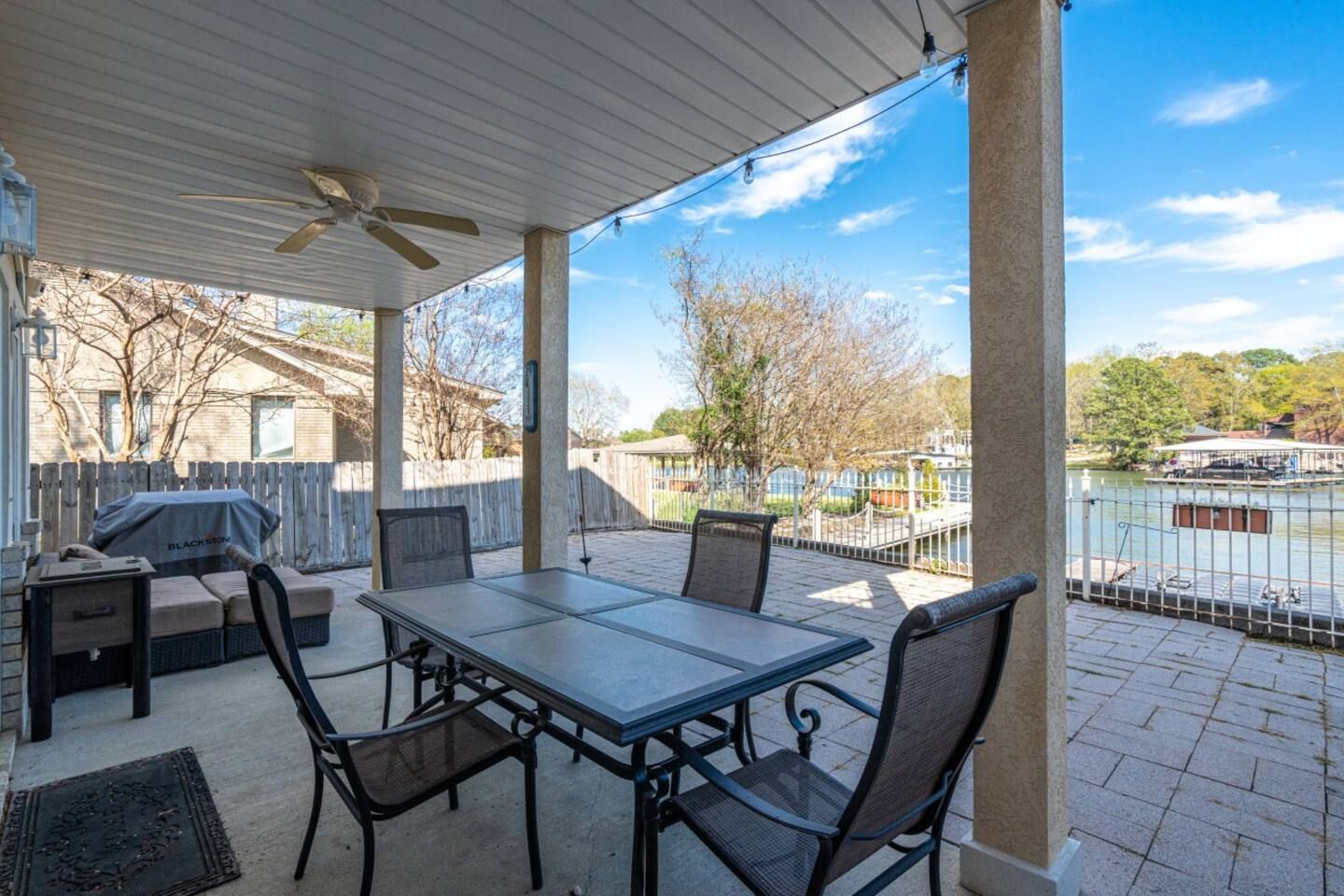 A patio with a table and chairs and a ceiling fan overlooking a lake.