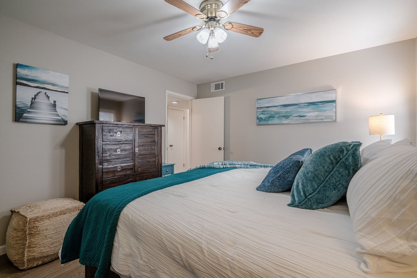 A bedroom with a bed , dresser , television and ceiling fan.