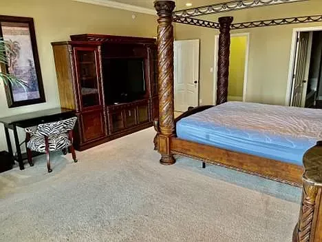 A bedroom with a four poster bed , television , desk and chair.