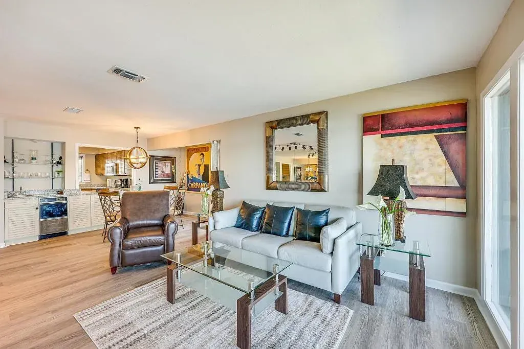 A living room with a couch , chair , coffee table and paintings on the wall.