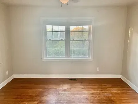 Empty room with a window, hardwood floor, beige walls, and white trim.