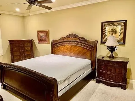 A bedroom with a bed , nightstand , dresser and ceiling fan.
