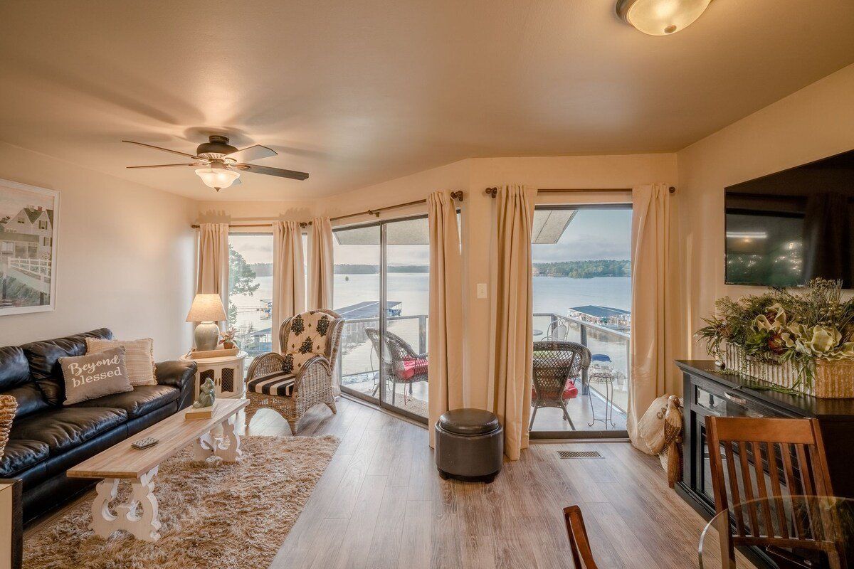 A living room with a couch , chairs , a television and a view of a lake.