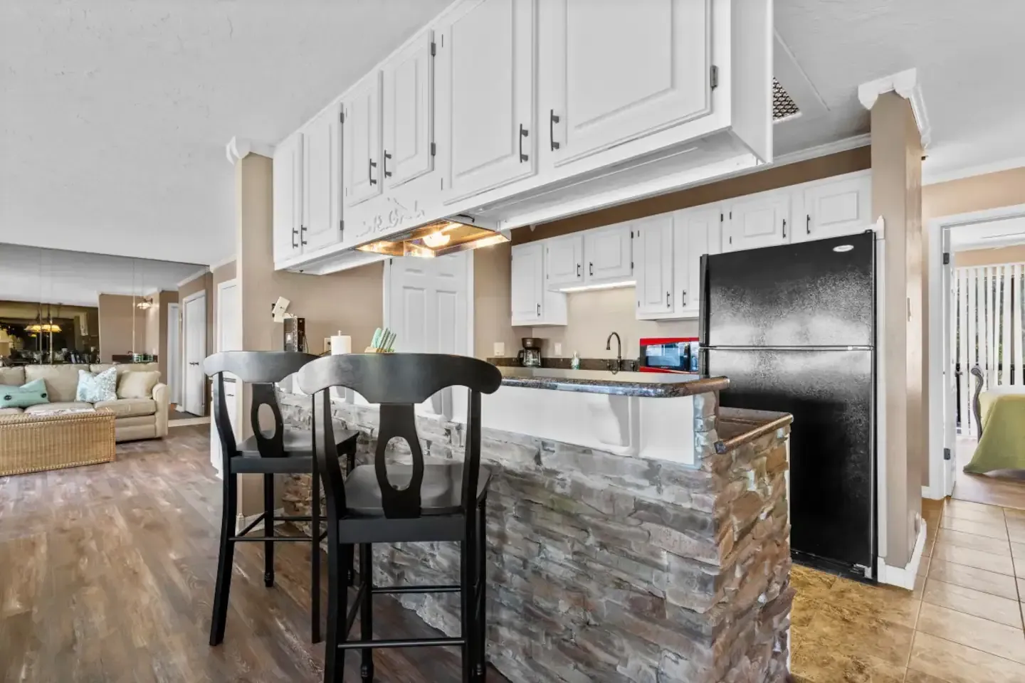 A kitchen with white cabinets , a black refrigerator , and a stone counter top.
