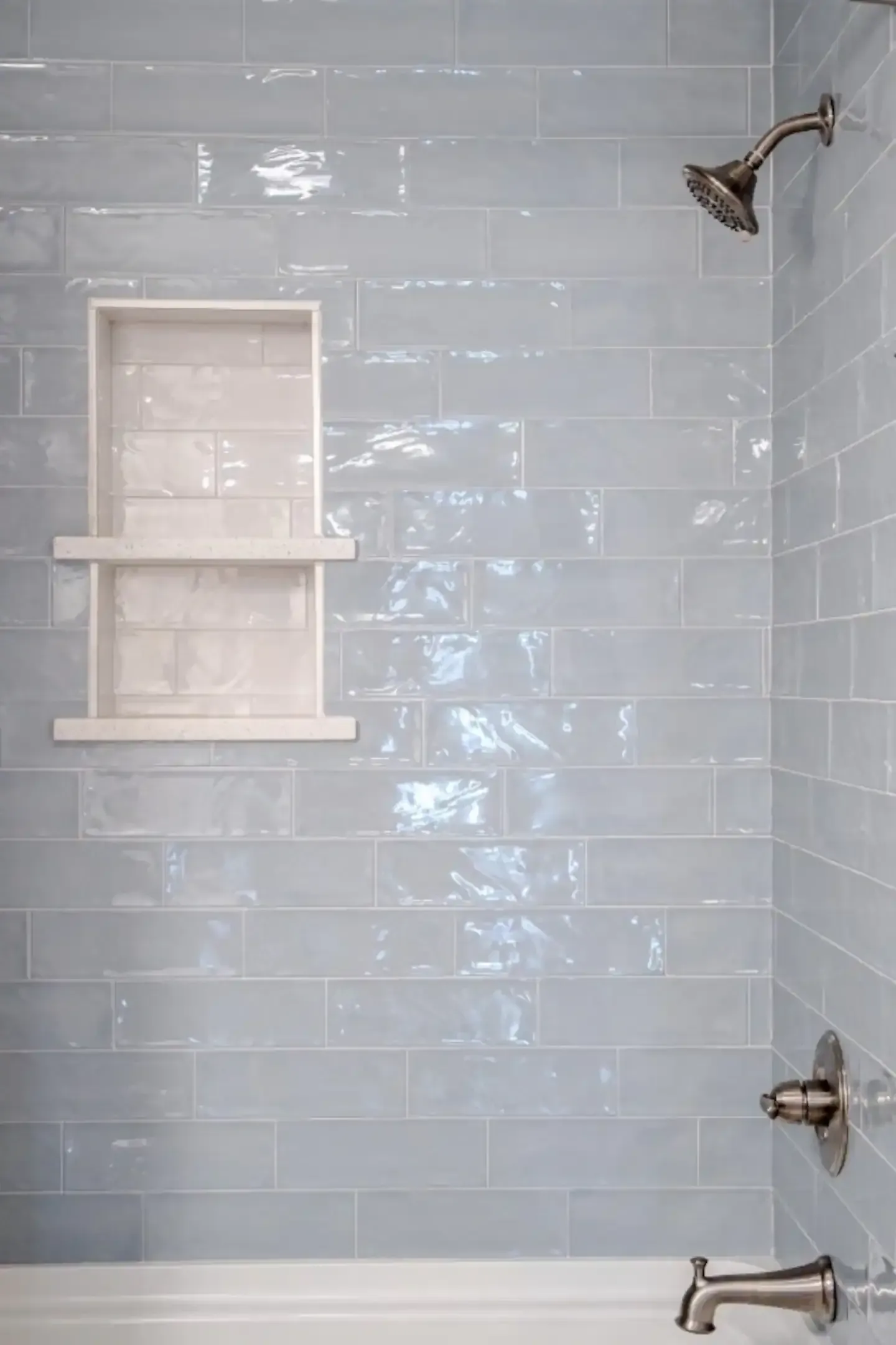 A bathroom with blue tiles , a bathtub , and a shower head.