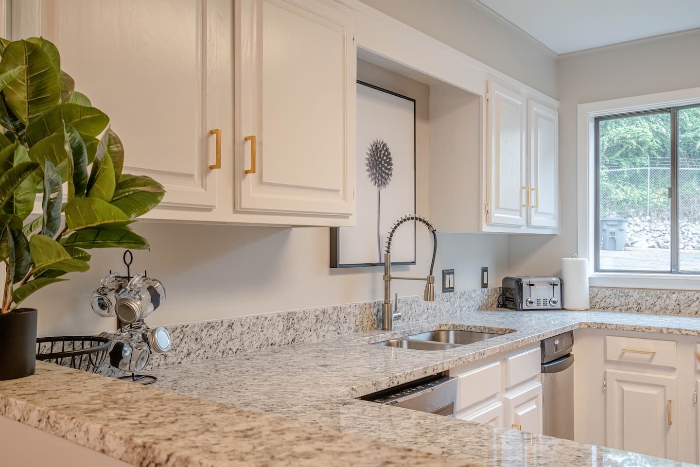 A kitchen with granite counter tops , white cabinets , a sink , and a window.