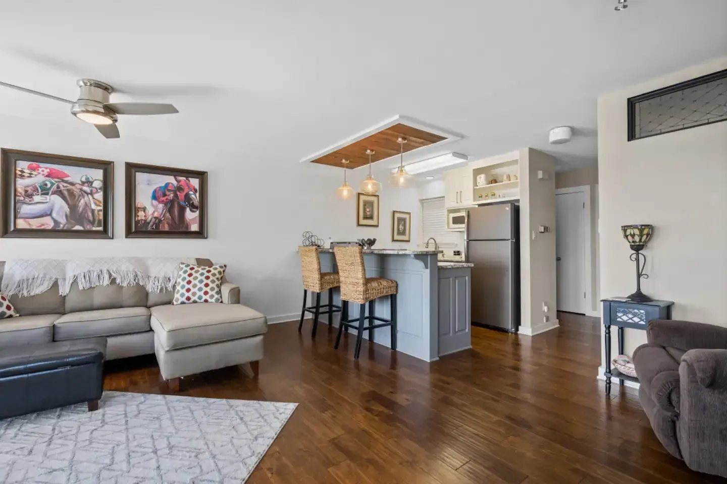 A living room with a couch , chairs , a ceiling fan and a kitchen.