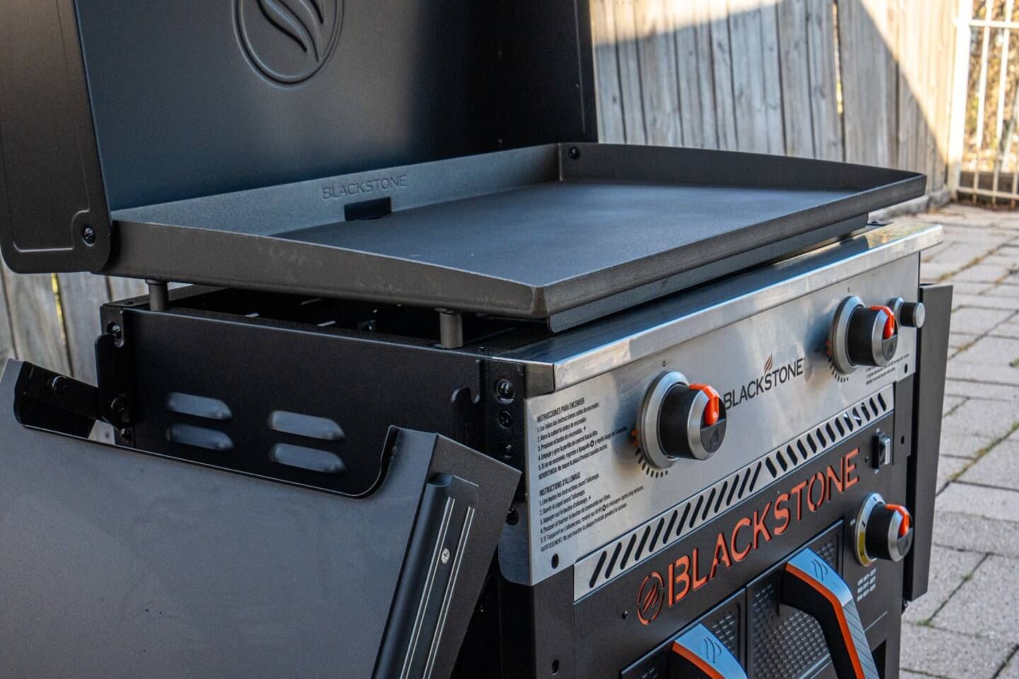 A grill with the lid open is sitting on a brick sidewalk.