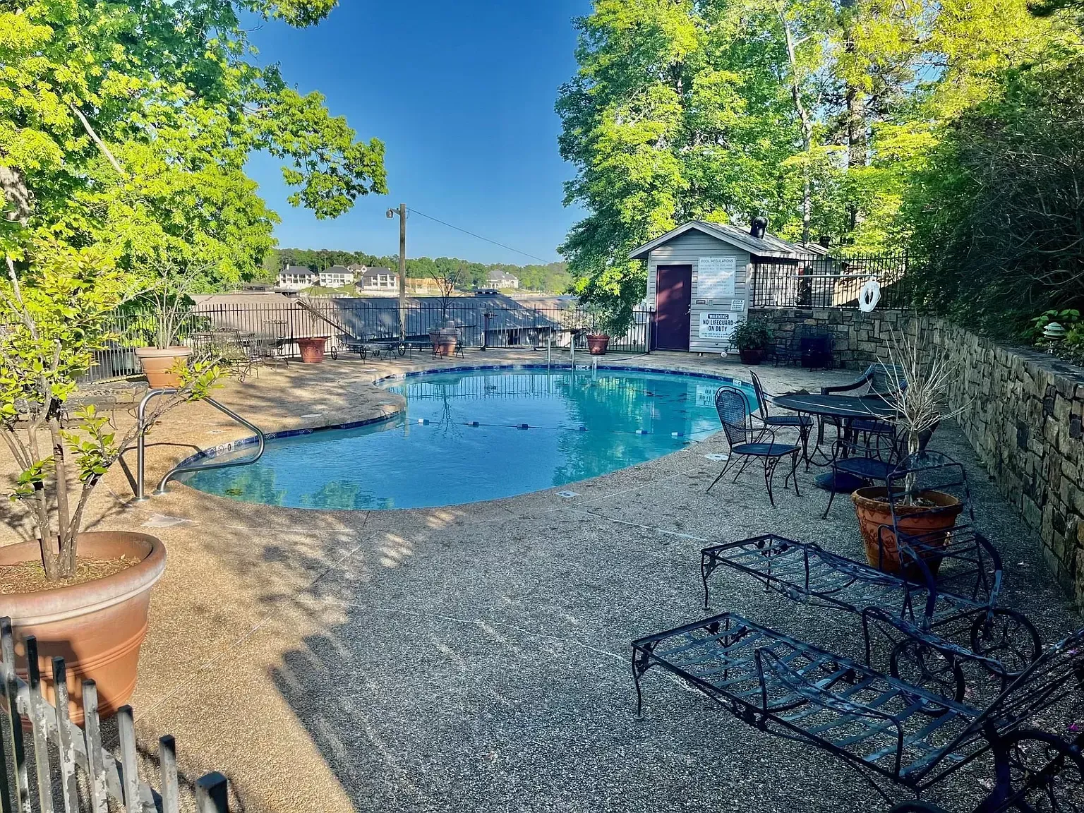 A large swimming pool is surrounded by a stone wall and chairs.