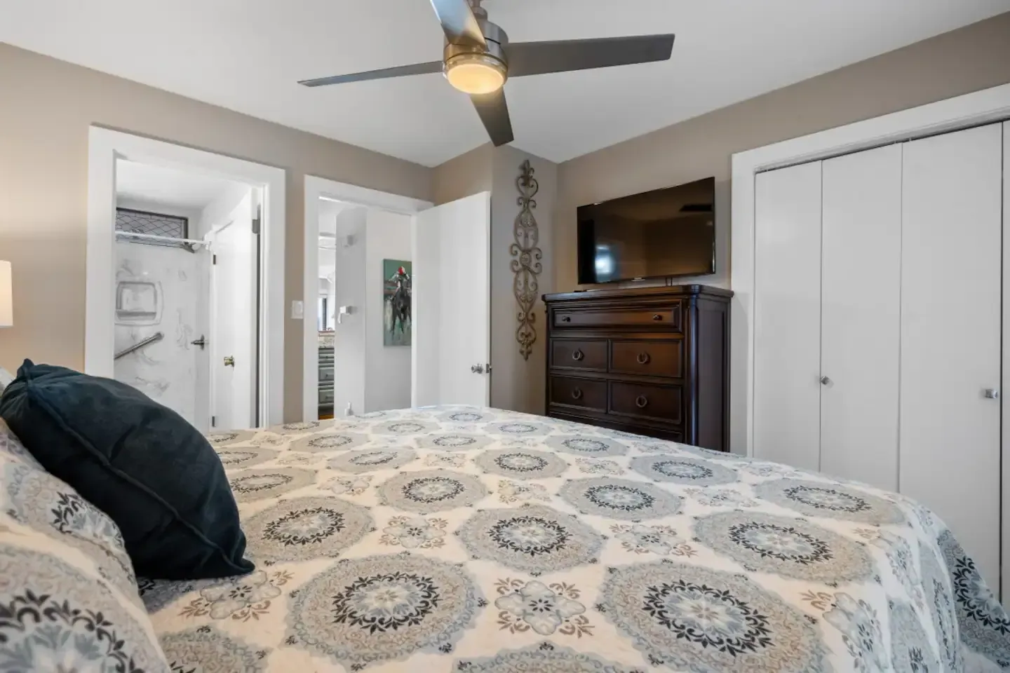 A bedroom with a bed , dresser , television and ceiling fan.