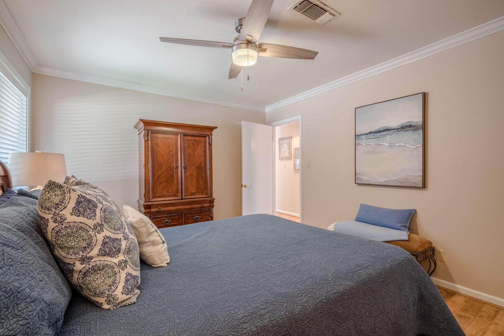 A bedroom with a king size bed , a ceiling fan , a wardrobe and a painting on the wall.