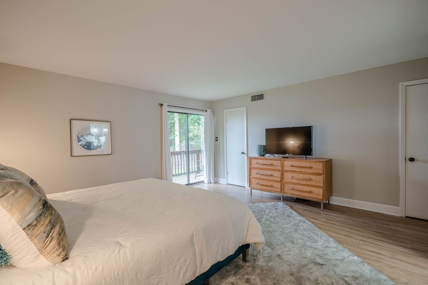 A bedroom with a bed , dresser , television and sliding glass doors.