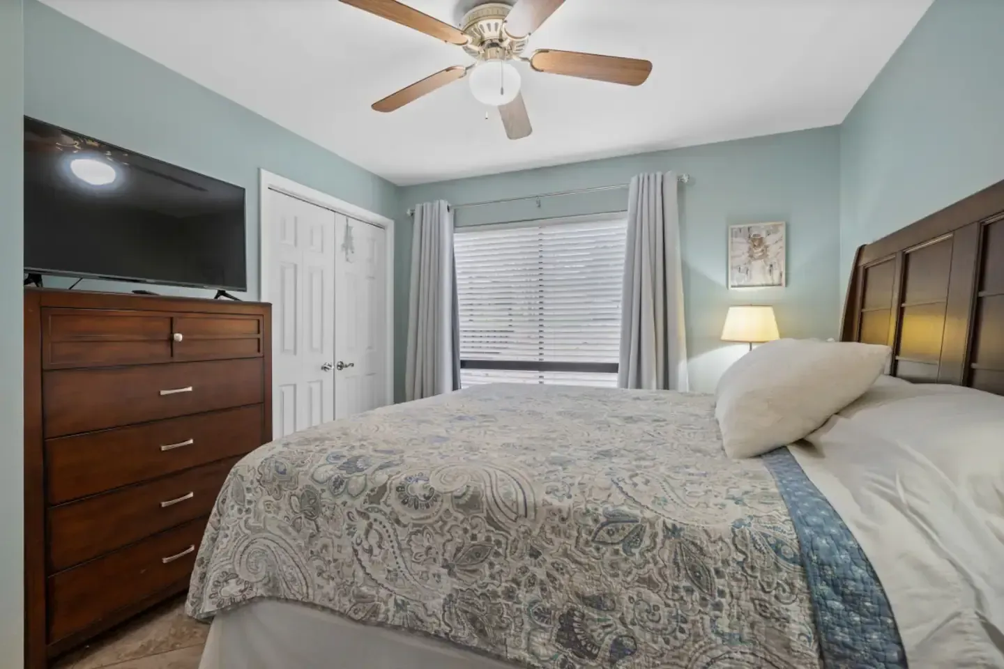 A bedroom with a bed , dresser , television and ceiling fan.