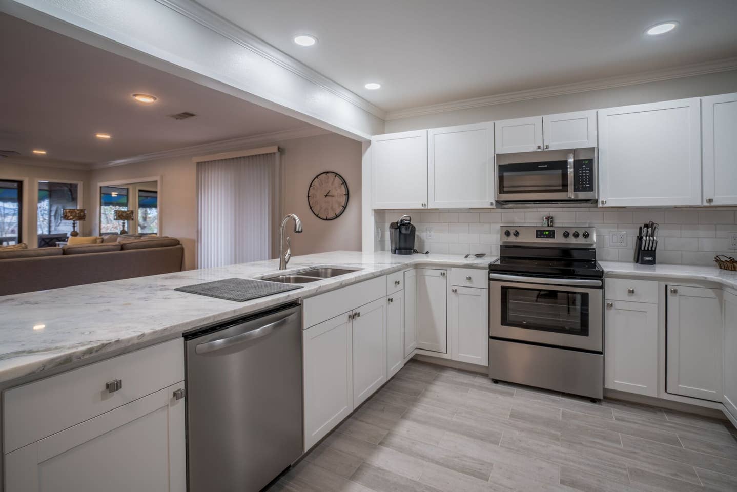 A kitchen with white cabinets , stainless steel appliances and a clock on the wall.