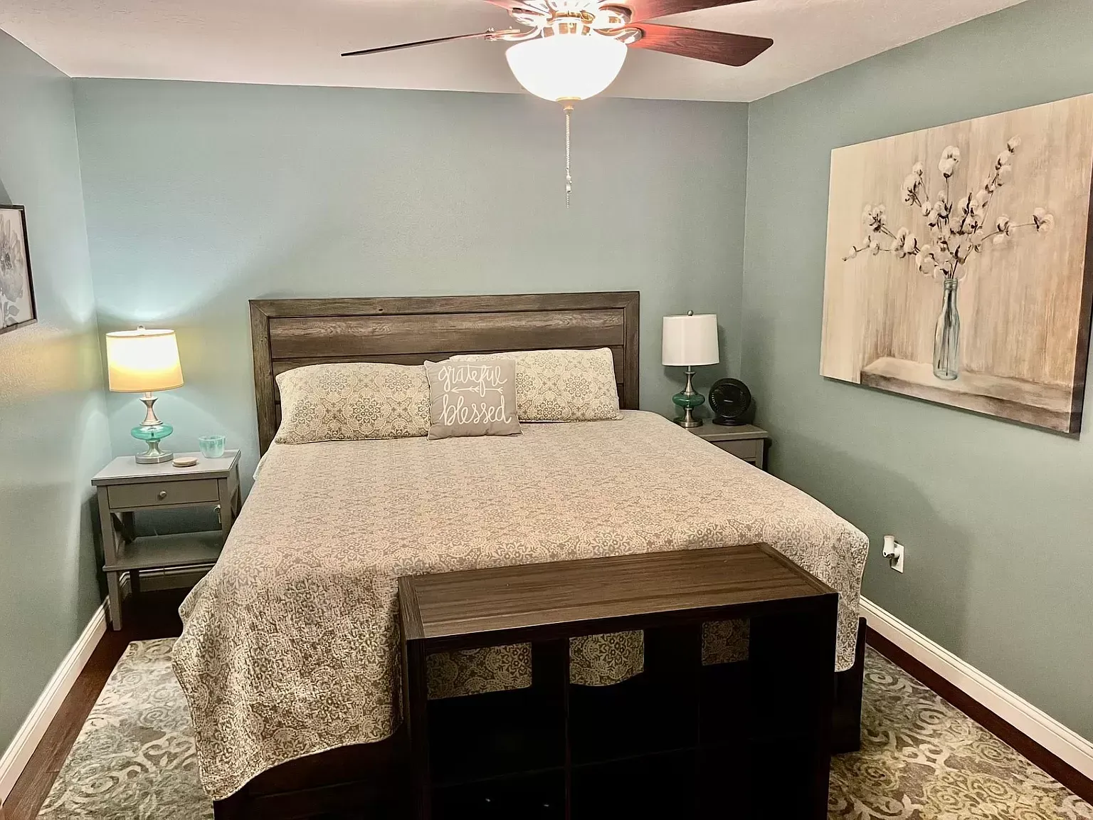 A bedroom with a bed , nightstand , lamp and ceiling fan.