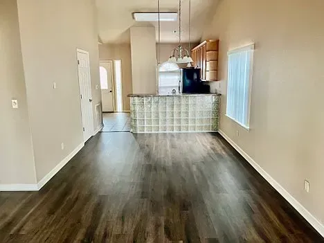 A living room with hardwood floors and a kitchen in the background.