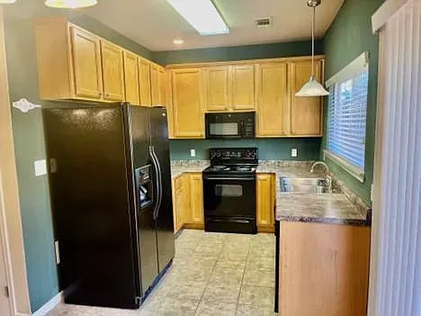 A kitchen with a black refrigerator , stove , microwave and sink.