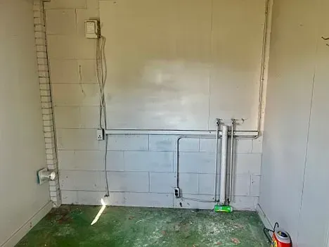 Interior wall with exposed plumbing and electrical wiring. Green floor and white block walls.