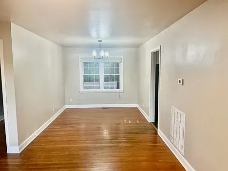 Empty dining room with hardwood floors, light gray walls, and a window.