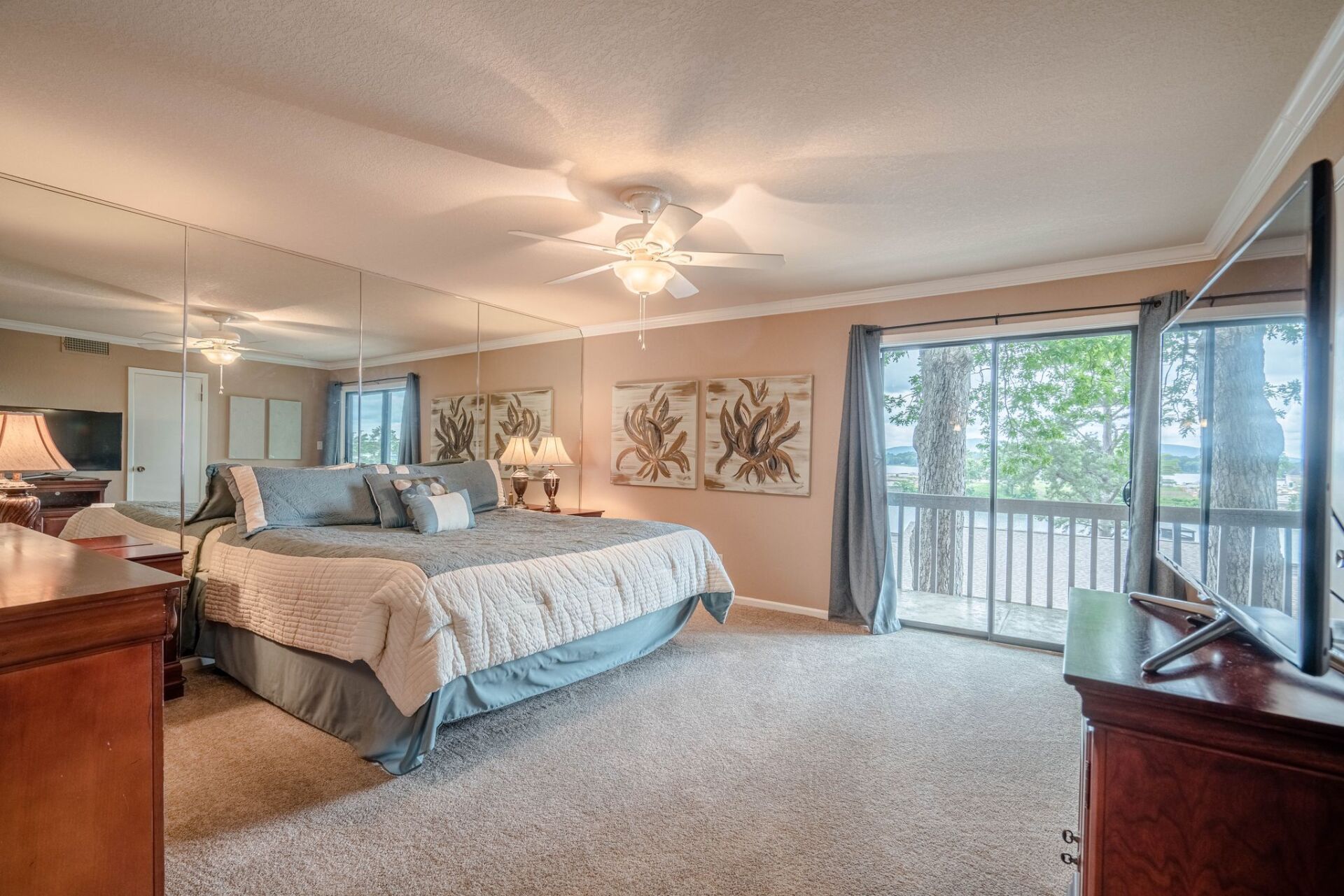 A large bedroom with a king size bed , dresser , television and sliding glass doors.