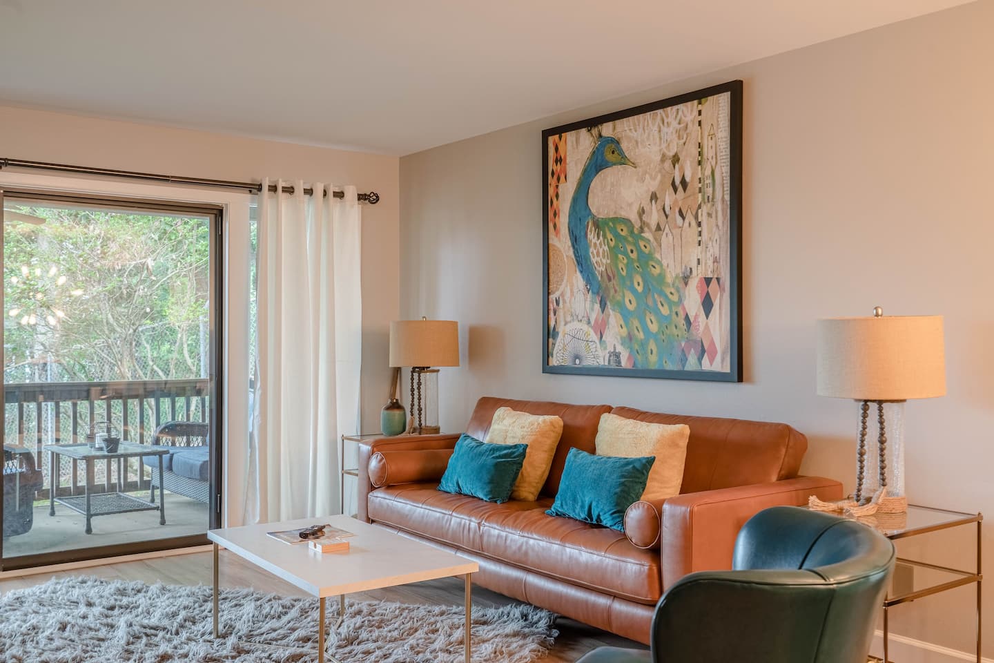 A living room with a couch , chair , coffee table and a peacock painting on the wall.