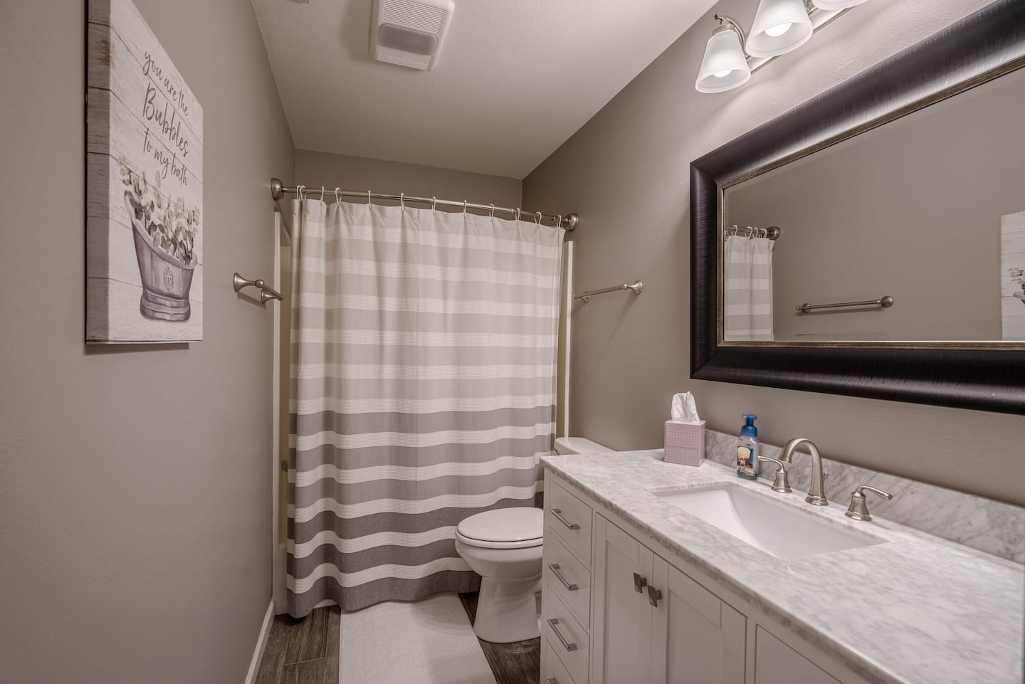 A bathroom with a toilet , sink , mirror and shower curtain.