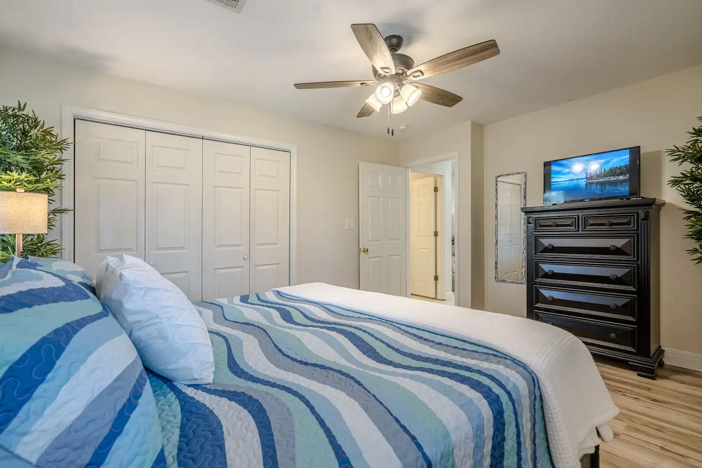 A bedroom with a bed , dresser , television and ceiling fan.
