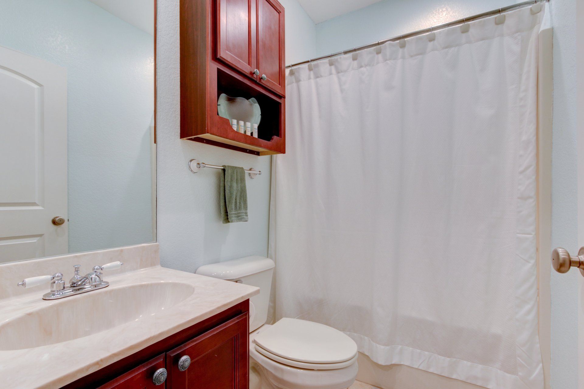 A bathroom with a toilet , sink , mirror and shower curtain.