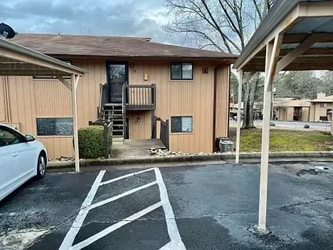 A white car is parked in front of a wooden apartment building.