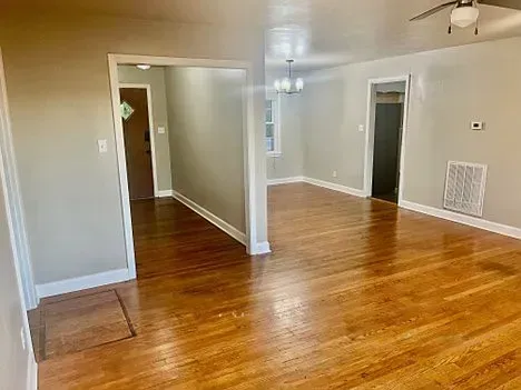 Hardwood floors in a house. Entryway to living room and other rooms are visible. Light gray walls.