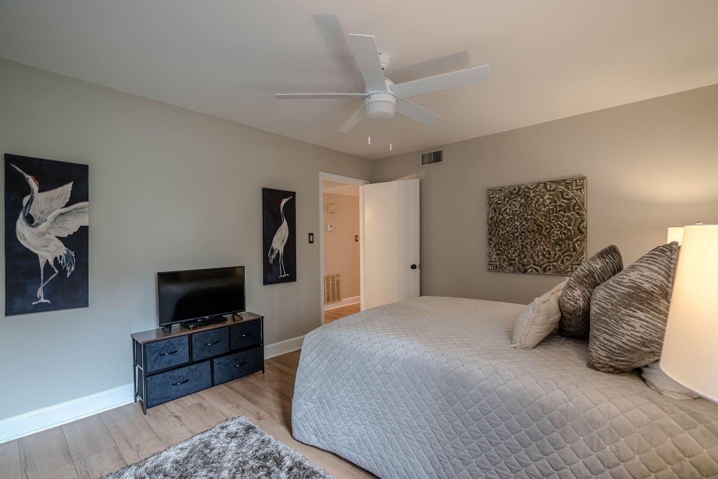 A bedroom with a bed , television , dresser and ceiling fan.