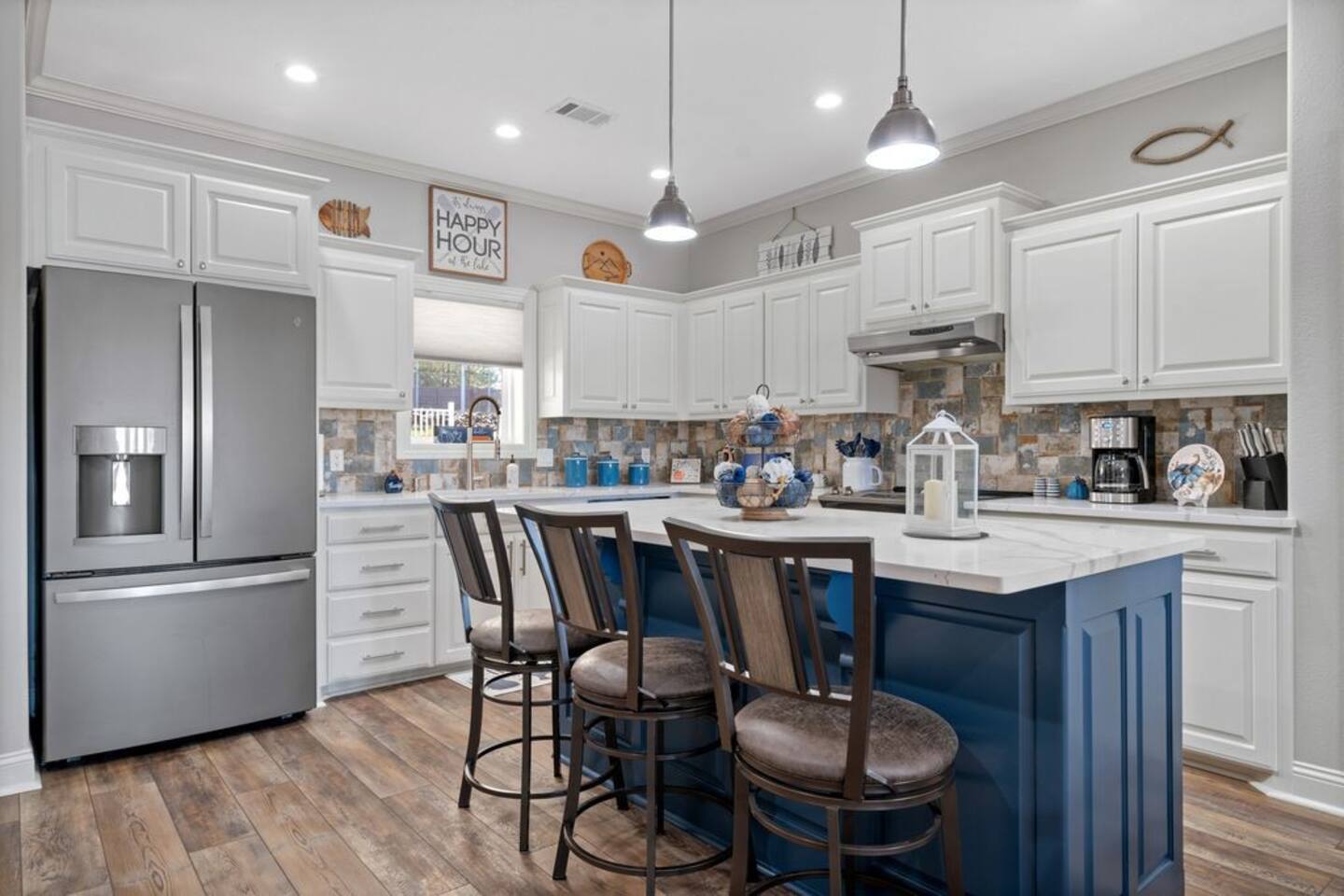 A kitchen with a blue island , white cabinets , stainless steel appliances and a refrigerator.