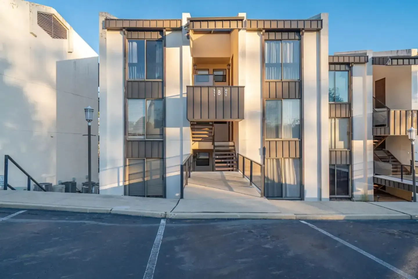 A large apartment building with stairs and a parking lot in front of it.