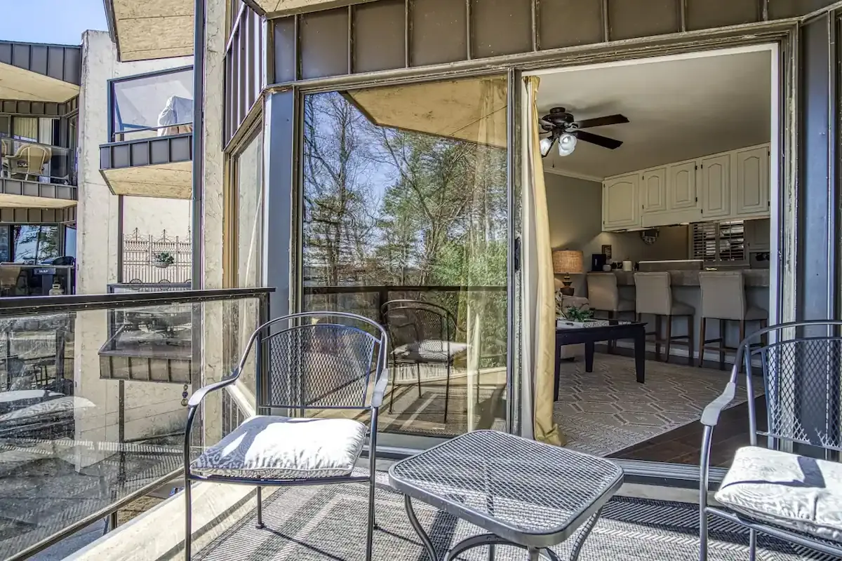 A balcony with a table and chairs and a sliding glass door leading to a living room.