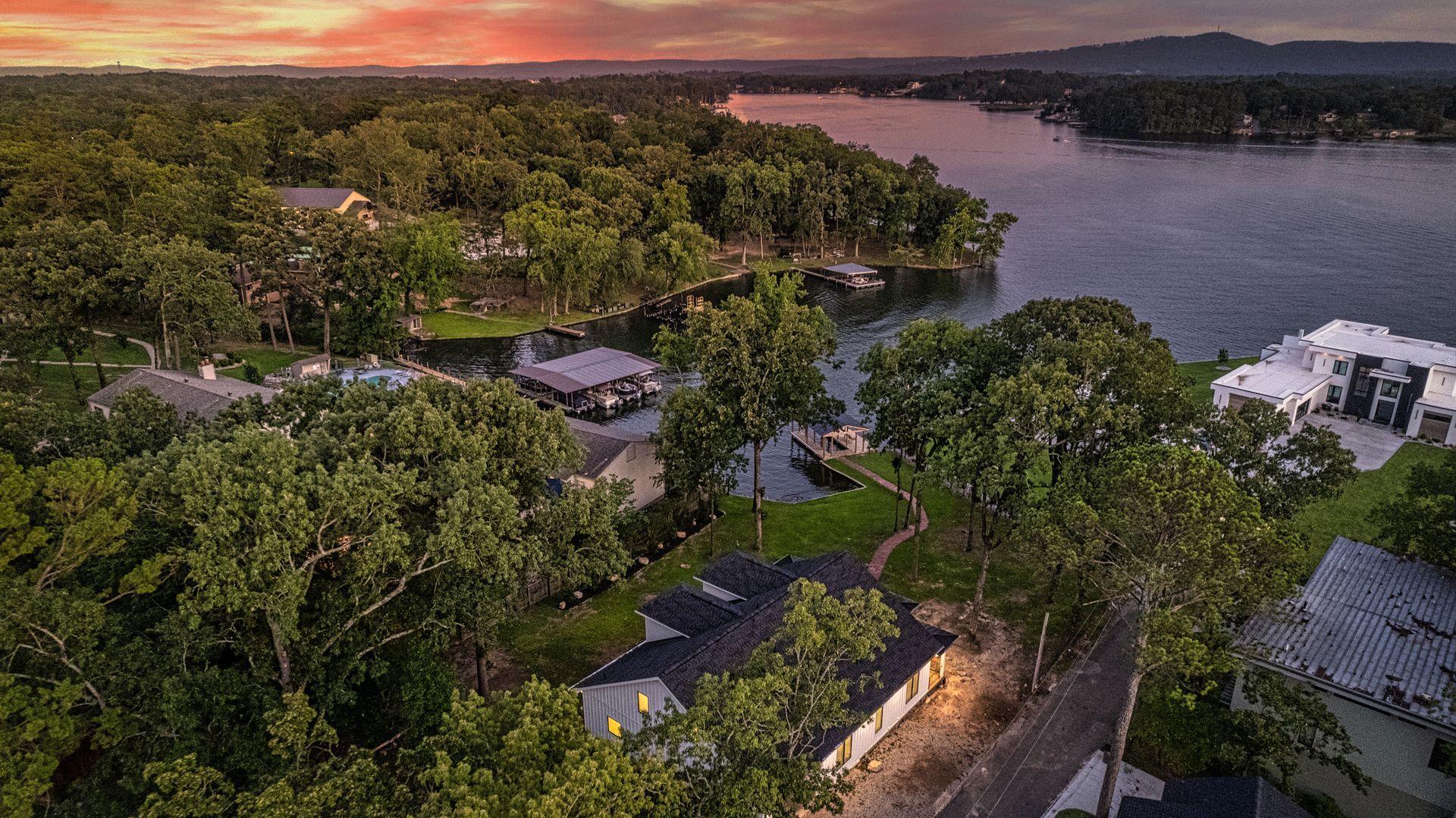 An aerial view of a lake surrounded by trees and houses at sunset.