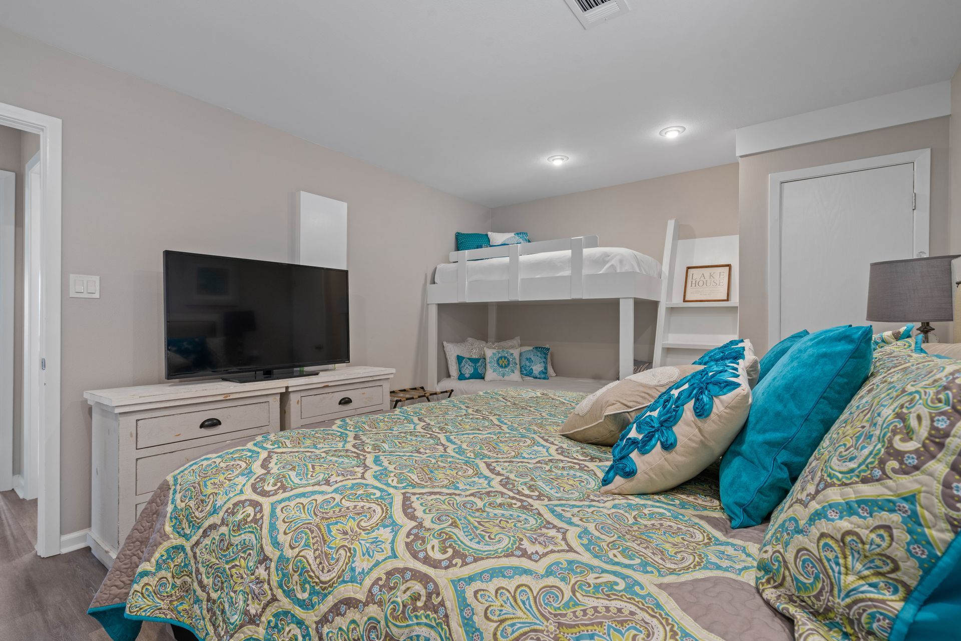 A bedroom with a king size bed , bunk beds , a flat screen tv and a dresser.