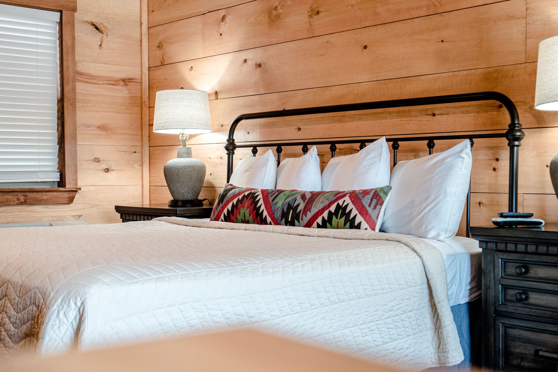 A bedroom with a bed , lamps , nightstands and a wooden wall.