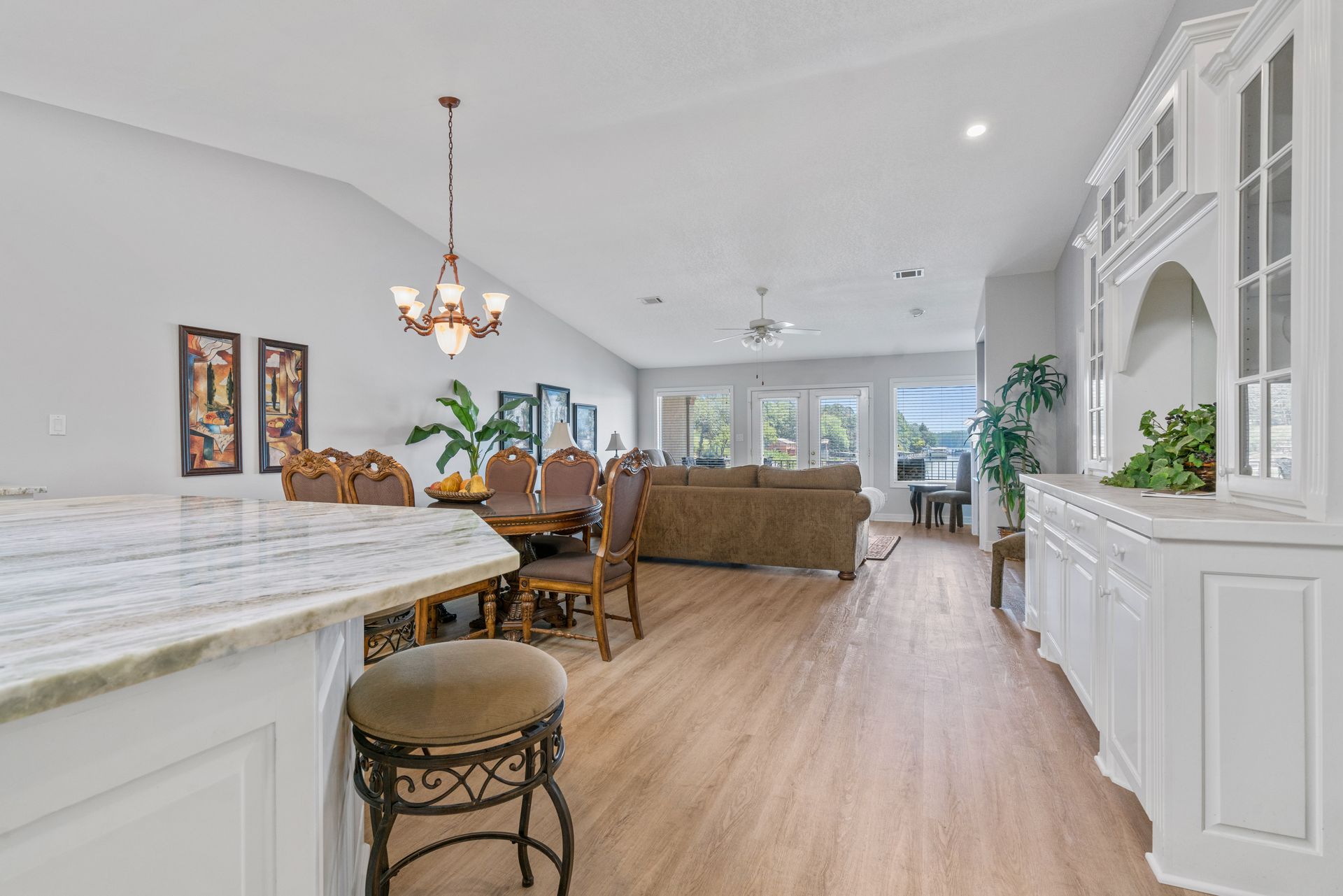 A kitchen with a marble counter top and wooden floors leading to a living room and dining room.