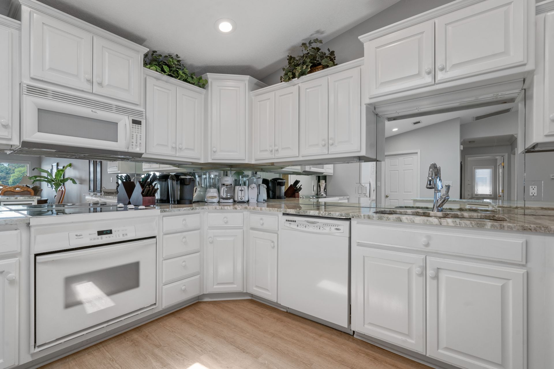 A kitchen with white cabinets , white appliances , a sink , and a mirror.
