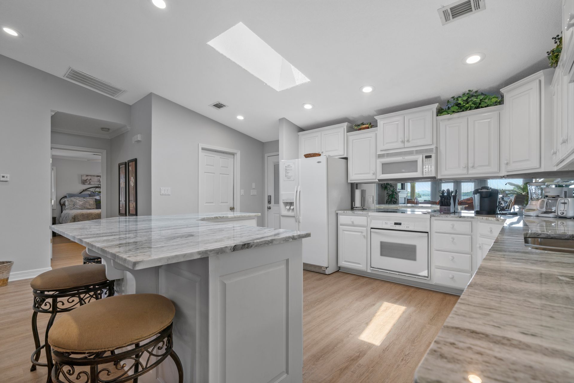 A kitchen with white cabinets , granite counter tops , stools and a large island.