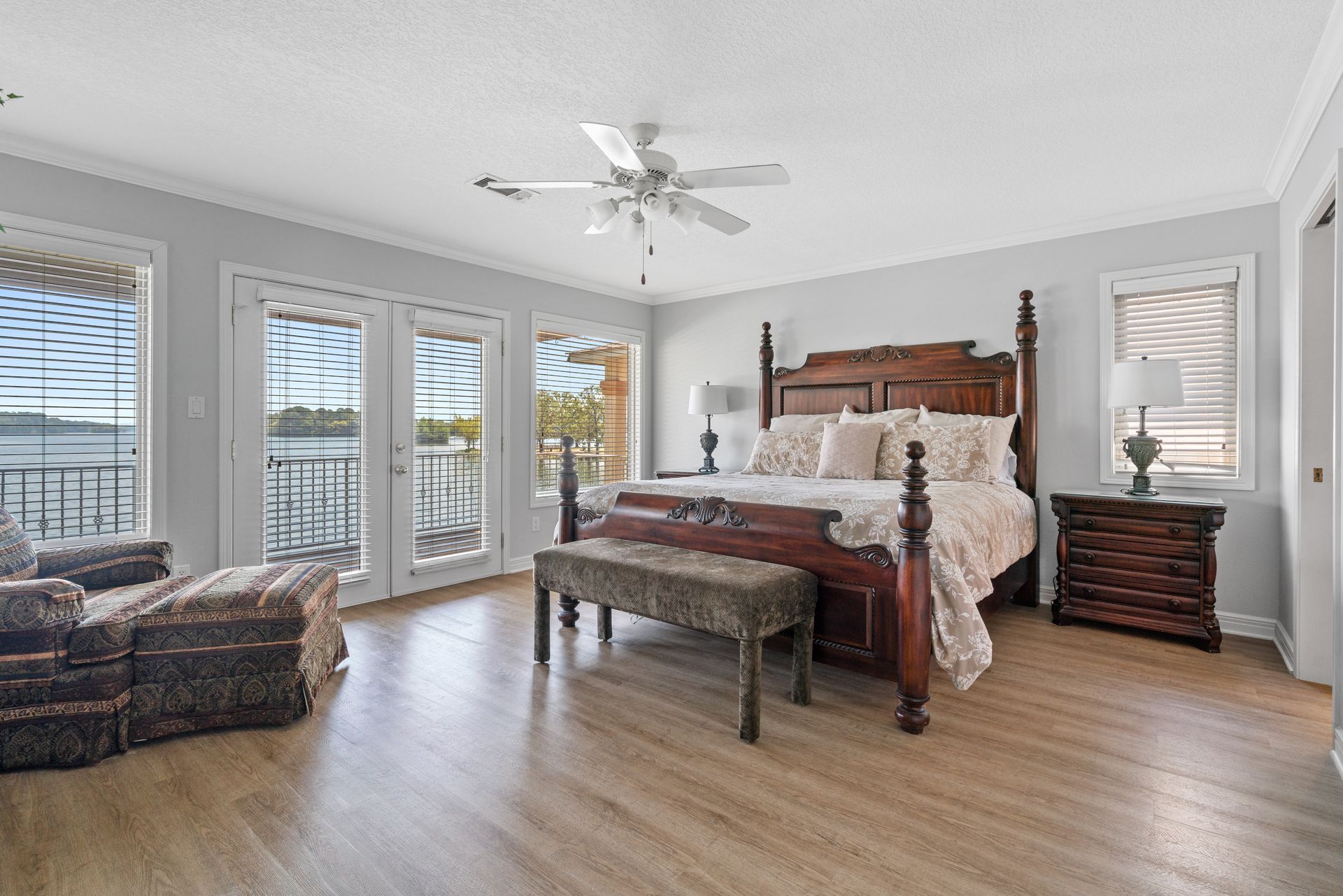 A bedroom with a king size bed , a bench , a chair and a ceiling fan.