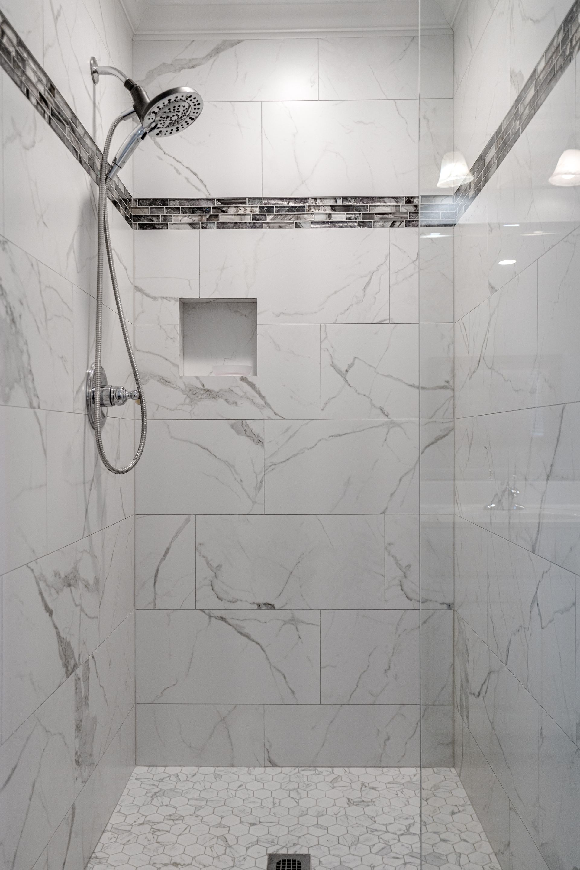 A walk in shower with marble tiles and a glass door.