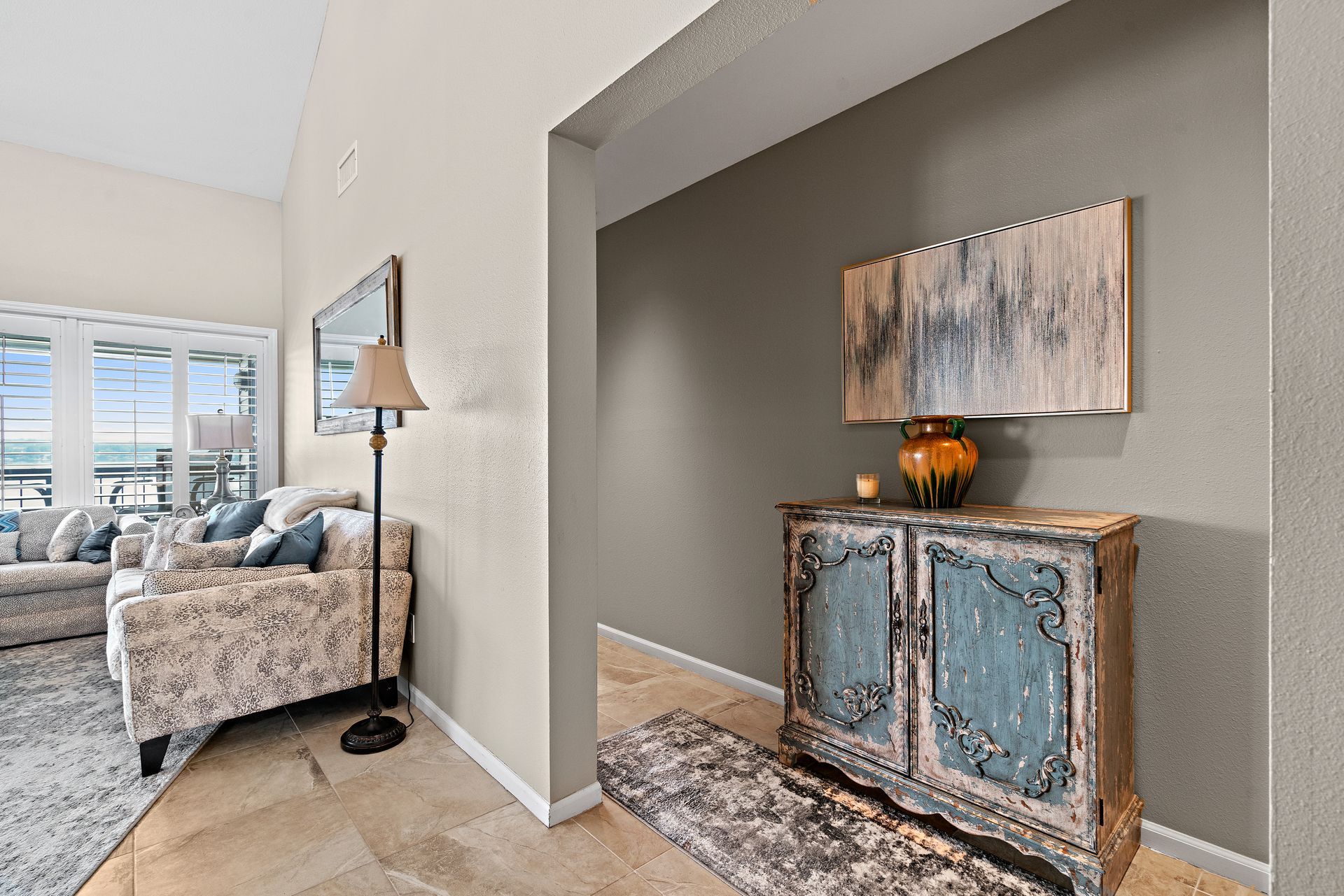 A living room with a couch , chair , lamp and dresser.