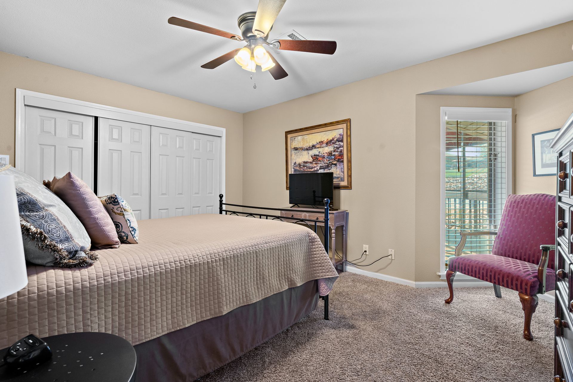 A bedroom with a bed , chair , ceiling fan and television.