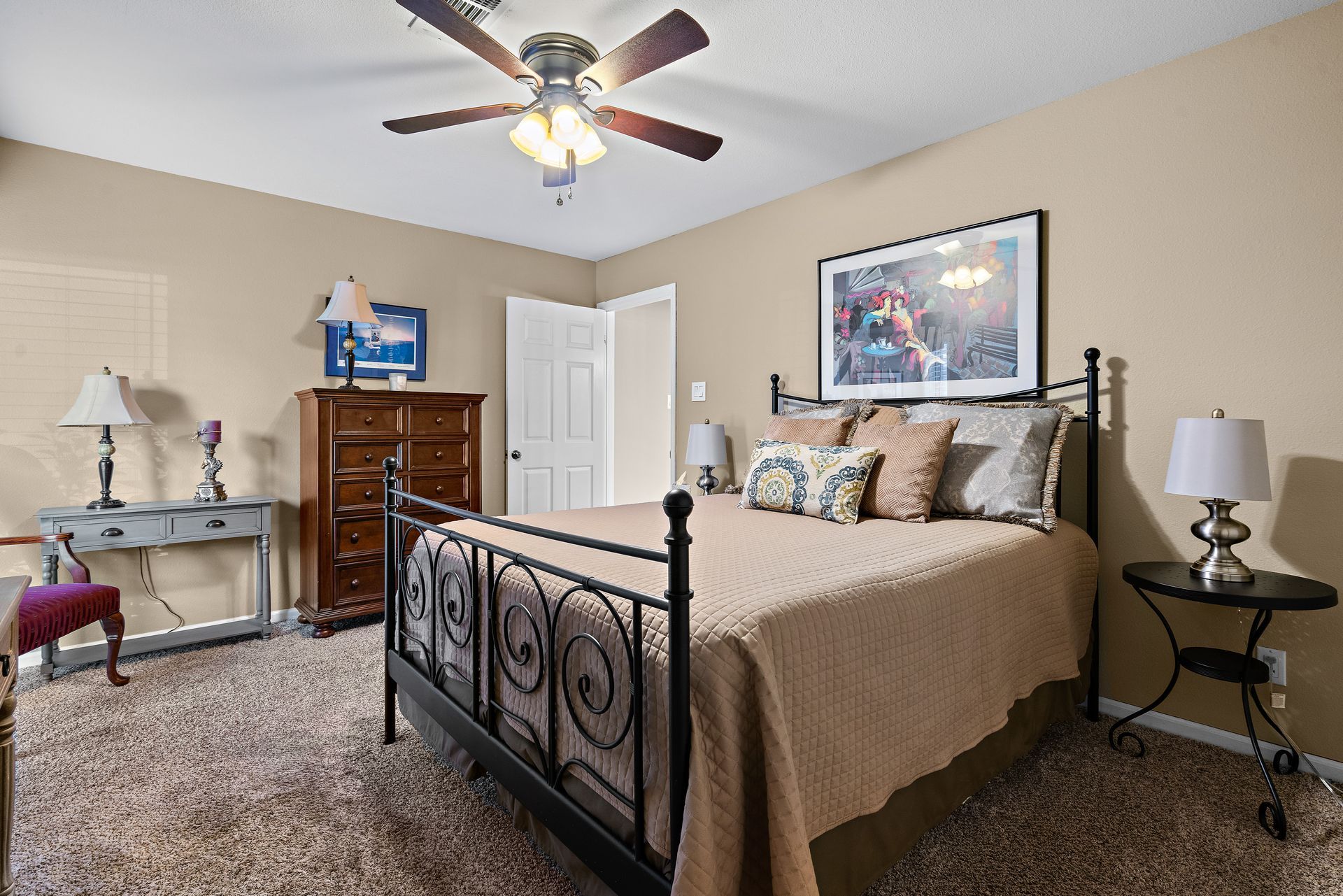 A bedroom with a bed , dresser , lamps and a ceiling fan.